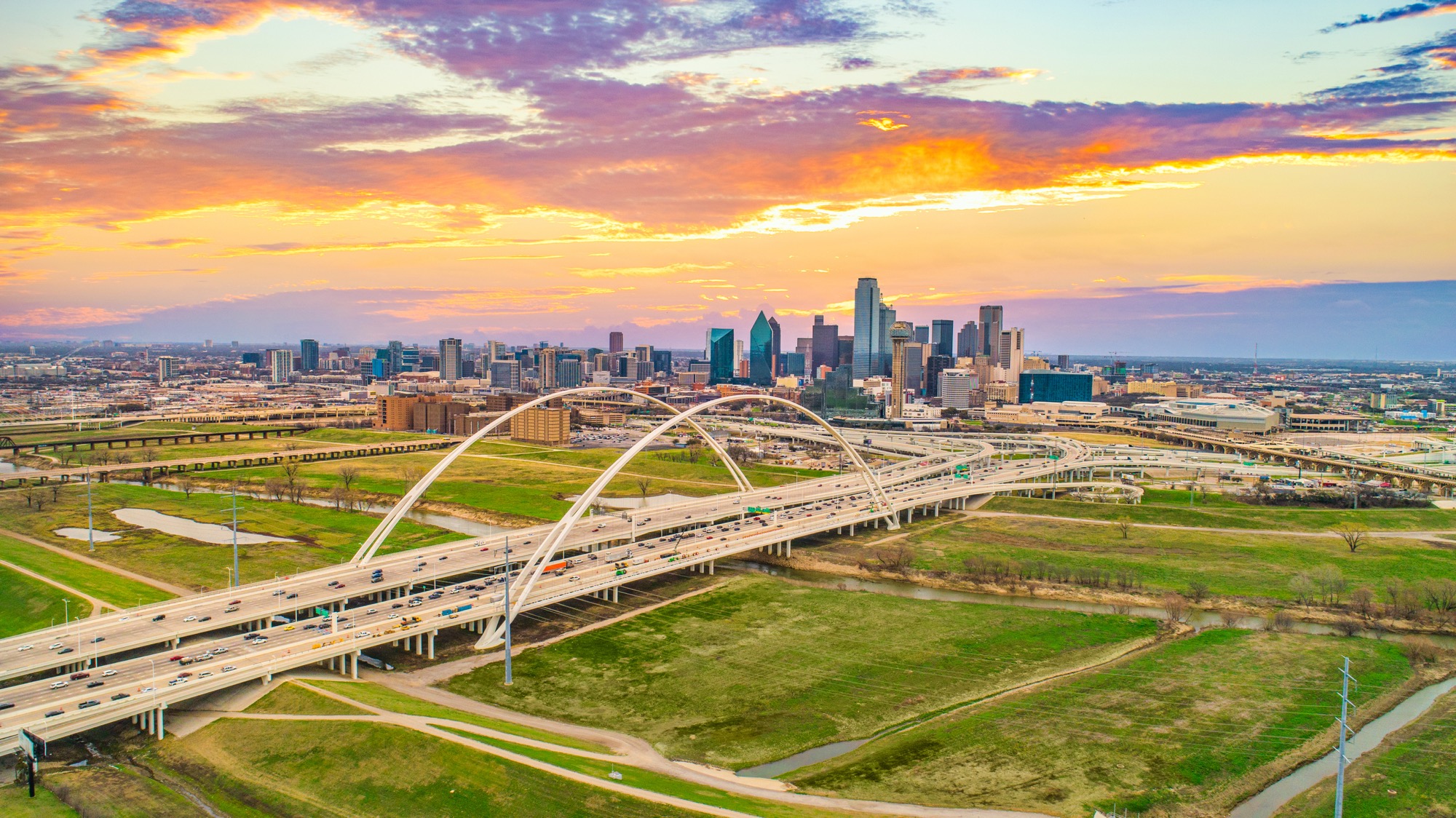 Aerial view of the Dallas skyline and Margaret McDermott Bridge at sunset, highlighting the city’s rapid growth