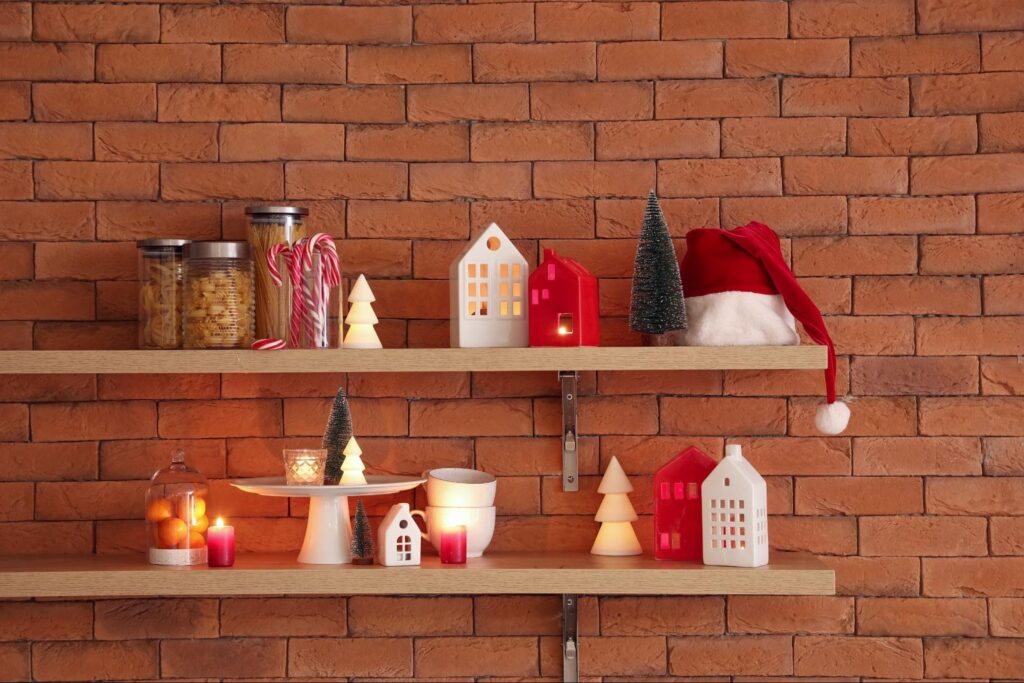 Floating shelves decorated with Christmas decor, including candles, a Santa hat, and festive treats on a brick wall. ©Pixel-Shot