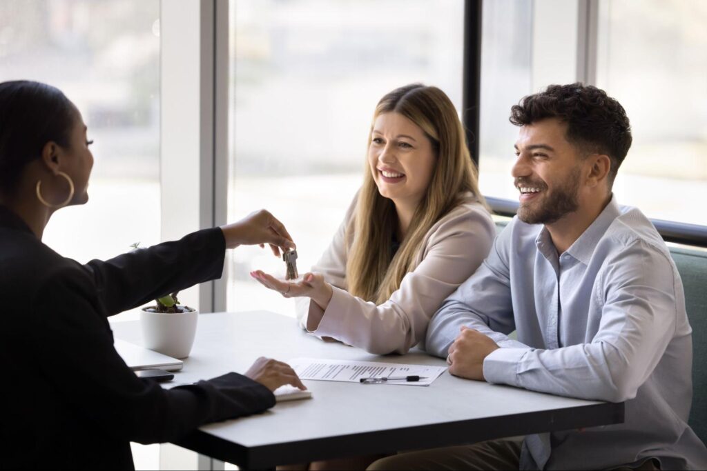 Happy couple reviewing home purchase documents at a table with keys ©fizkes