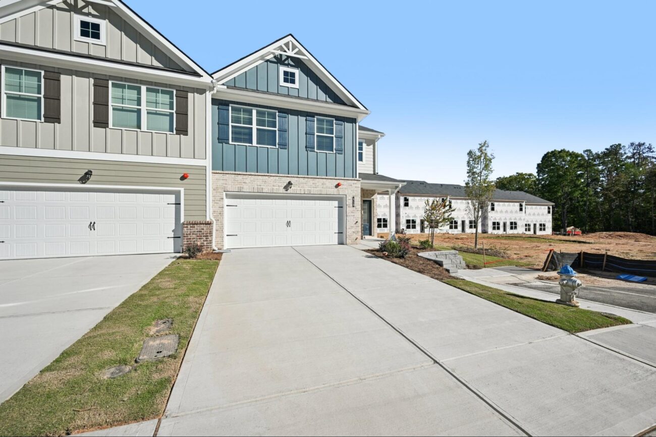 A row of modern, newly constructed two-story townhomes featuring blue and grey siding with stone accents and two-car garages.