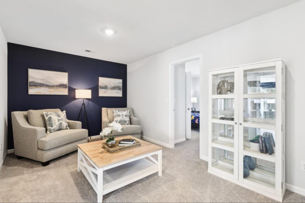 Finished basement sitting room in a new construction home with armchairs, coffee table, and display cabinet.